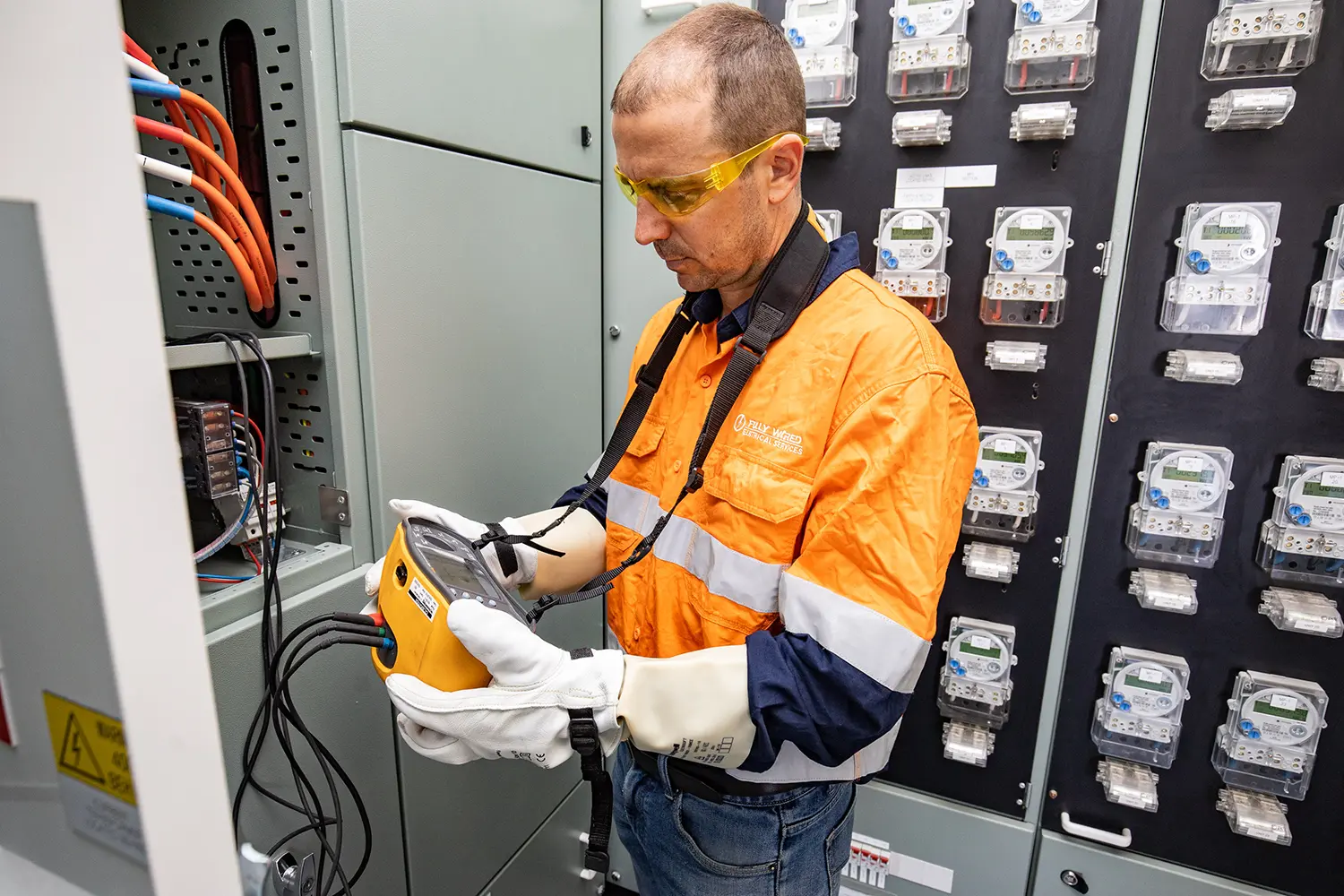 Fully Wired electrician in hi-vis carrying out an electrical compliance inspection in a unit complex meter room
