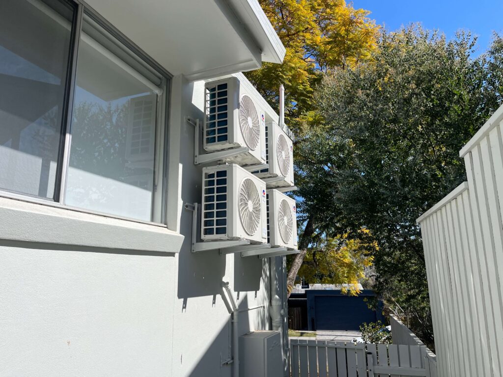 Four air conditioner outdoor units grouped neatly at the back of an Indooroopilly home