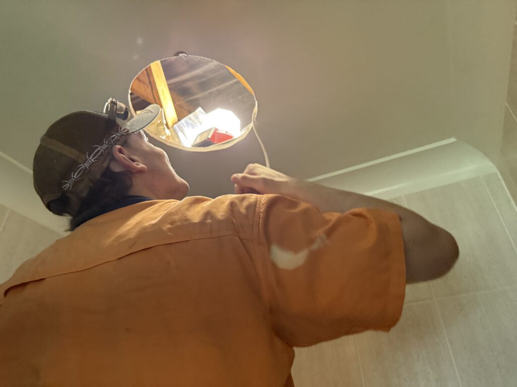 Electrician fitting a ceiling-mounted fan unit in a Brisbane bathroom