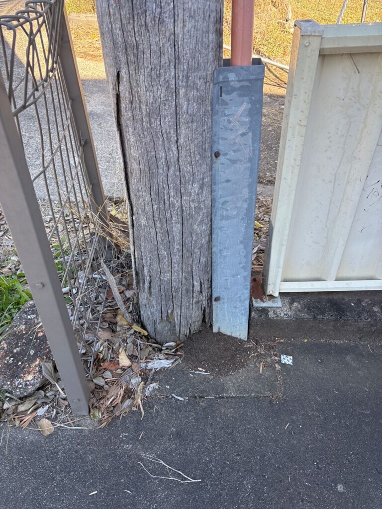 Base of an ageing timber property pole set in concrete and pavers in Booval