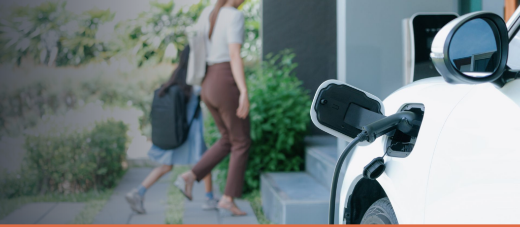 Electric car plugged into a wall-mounted home charger beside a garden path